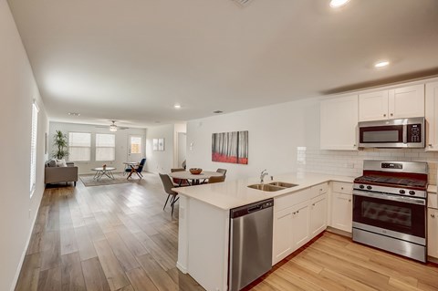 Open concept kitchen seamlessly blending into the dining and living areas, featuring white cabinetry and hardwood floors for a clean and cohesive design