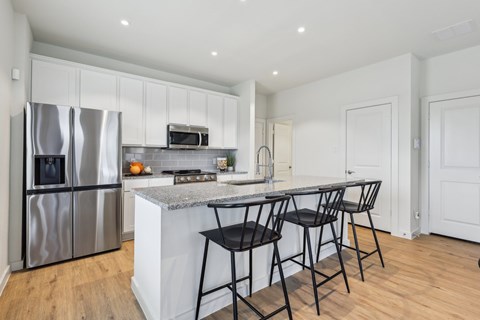 A kitchen with a refrigerator, microwave, and bar stools.
