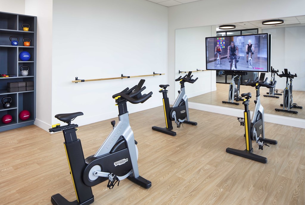Spin Studio Room with Mirrored Wall, Flat Screen TV, and Plank Flooring at North+Vine Apartments in Chicago, IL