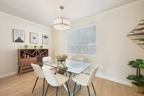 A dining room with a glass table and white chairs.