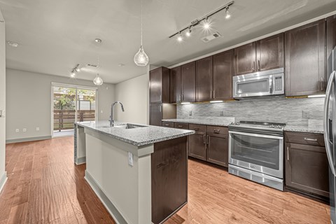 A modern kitchen with dark brown cabinets and a wooden floor.