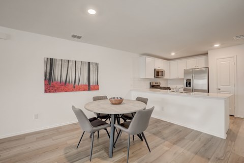 Open concept kitchen seamlessly blending into the dining and living areas, featuring white cabinetry and hardwood floors for a clean and cohesive design.