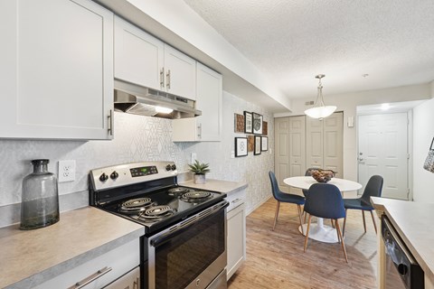 A kitchen with a stove top oven and a dining table with chairs.
