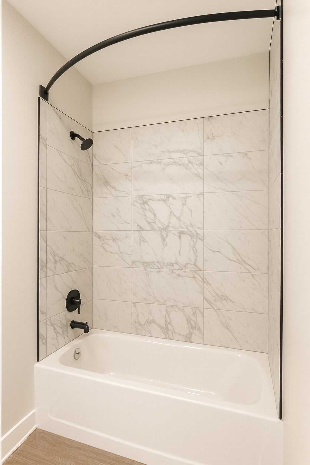 A white marble tiled shower with a black curved shower rod.