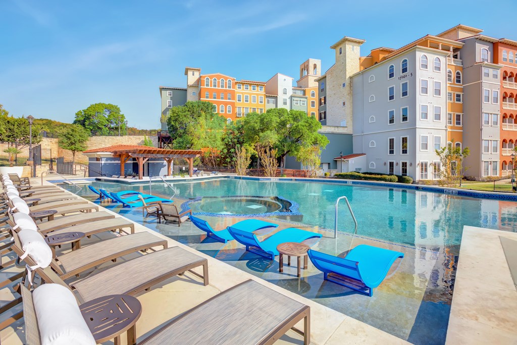 a swimming pool with blue lounge chairs and buildings in the background