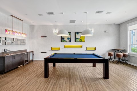 A pool table is in the middle of a room with a bar area to the left.