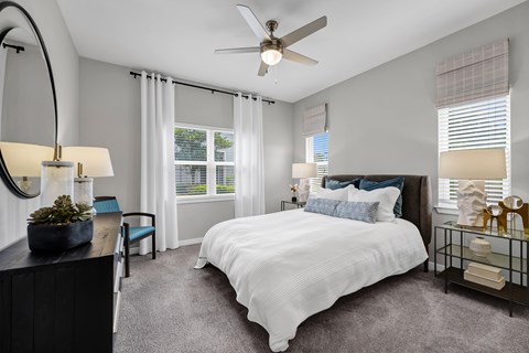 A bedroom with a large bed, a ceiling fan, and a window with blinds.