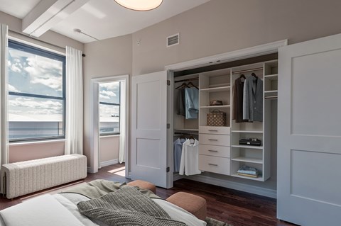 A bedroom with a large bed and a wardrobe with clothes hanging in it.