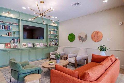 A living room with a green chair, orange couch, and a bookshelf filled with books.
