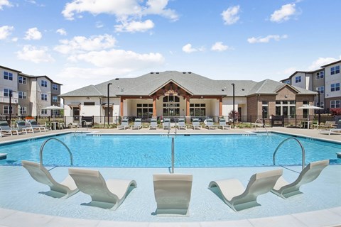 a swimming pool with chairs in front of an apartment building