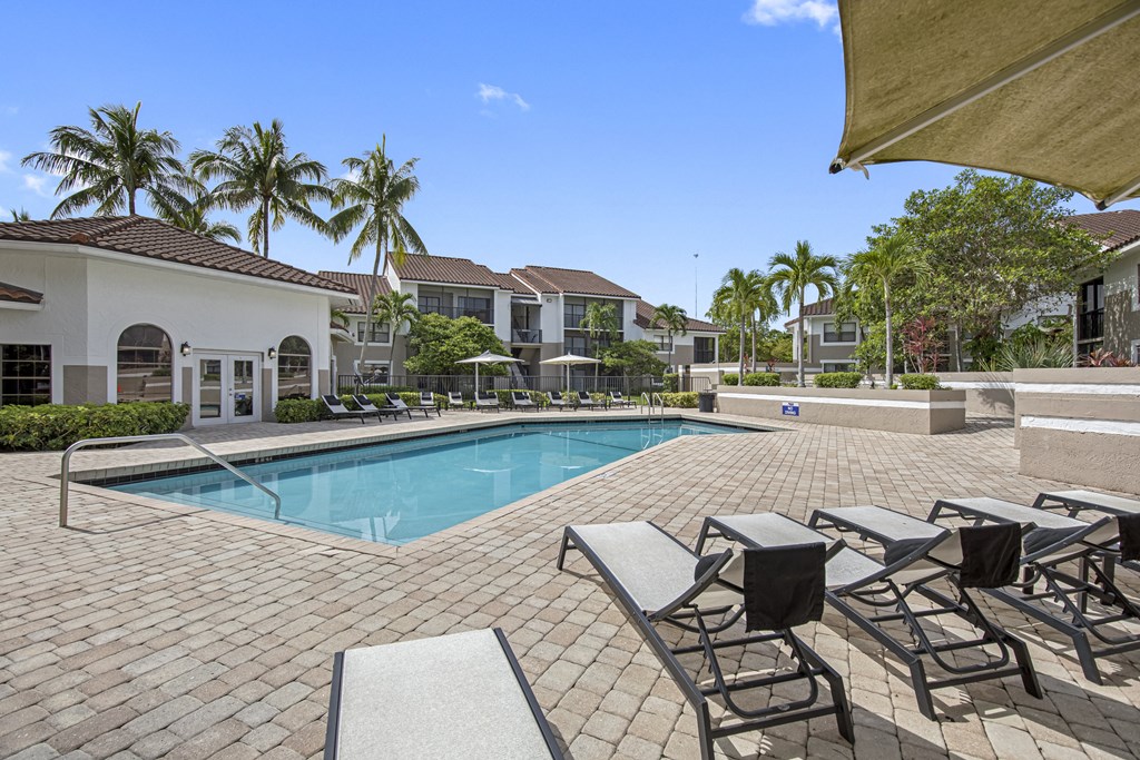 a resort style swimming pool with lounge chairs and umbrellas