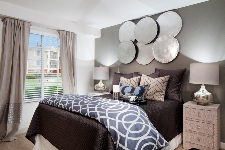 Ardenne Apartments bedroom with large windows, beigh drapes and queen sized bed with brown and blue bedding