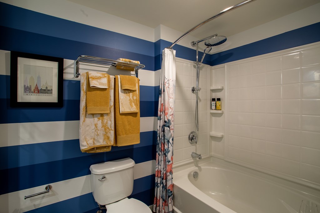 a bathroom with blue and white striped walls and a shower and a toilet and tub