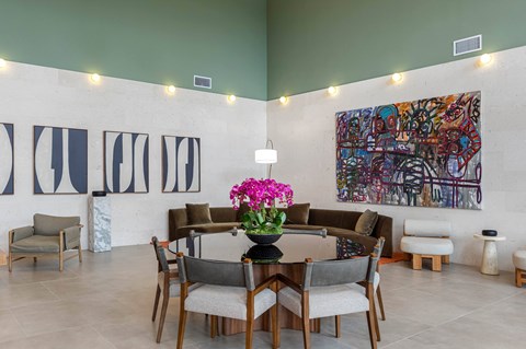 A dining room with a large painting on the wall and a table set with chairs and flowers.
