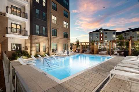 A swimming pool surrounded by lounge chairs in front of apartment buildings.