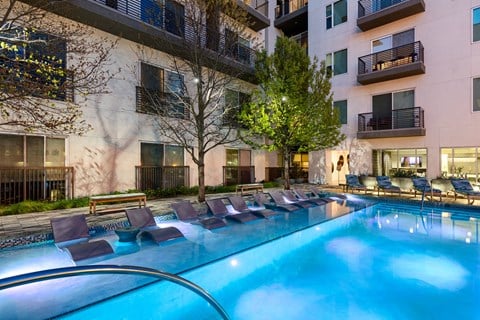 A swimming pool with lounge chairs and apartment buildings in the background.