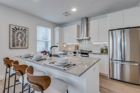 A modern kitchen with a stainless steel refrigerator and wooden bar stools.