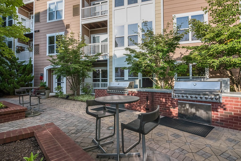 a patio with a grill and tables in front of an apartment building