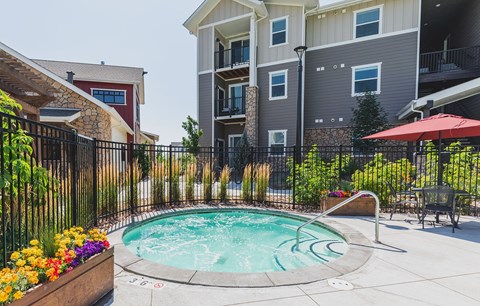 A hot tub sits in the middle of a patio surrounded by a black fence.