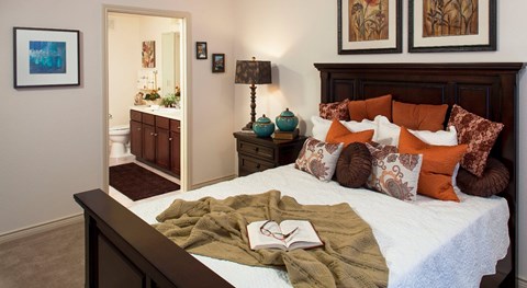 A bedroom with a bed, a lamp, a mirror, and a painting on the wall.