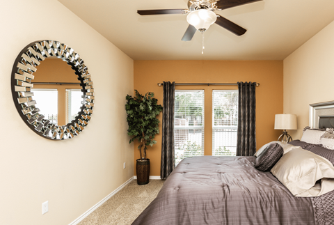 A bedroom with a bed, a mirror, a ceiling fan, and a potted plant.