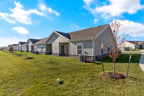 Two-Bedroom Senior Townhomes in Belton, MO - Traditions Villas 55+ - A Lawn Fronting a Row of Houses, and a Tree.