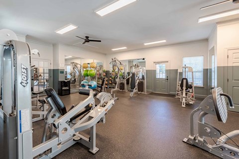 A spacious gym with a variety of equipment including treadmills, weight machines, and a ceiling fan.