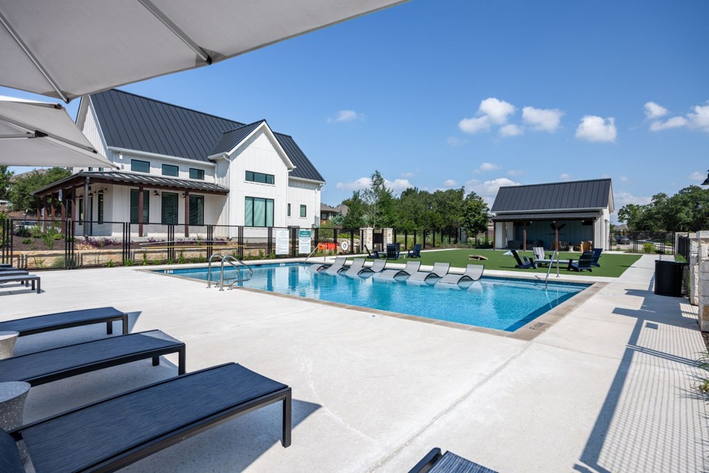 a swimming pool with chaise lounge chairs and sun umbrellas in front of a house