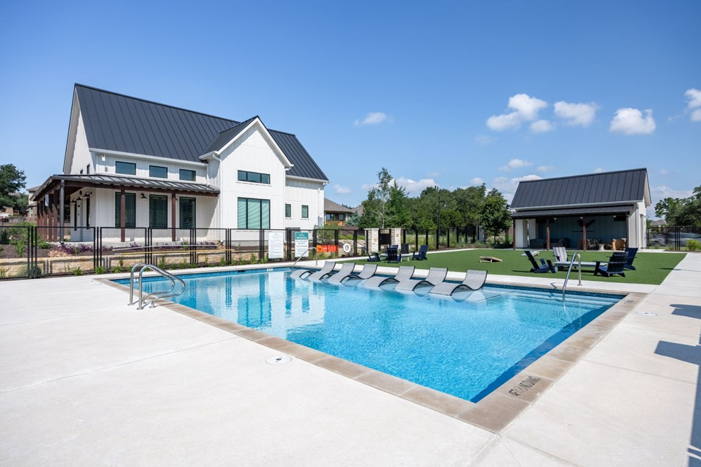 a swimming pool with chaise lounge chairs and a house in the background