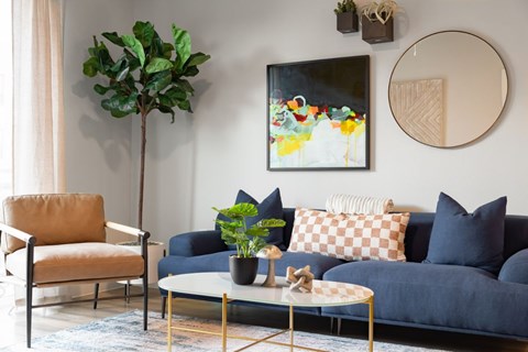 A living room with a blue couch, a chair, a coffee table, and a painting on the wall.