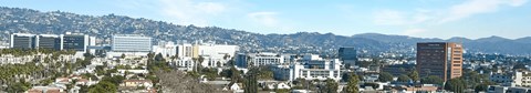 A cityscape with buildings and trees in the foreground and mountains in the background.