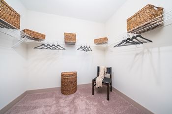 A room with a chair, a basket, and clothes hanging on a rack.
