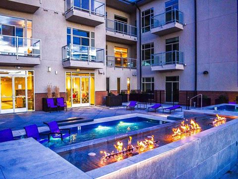 the pool is lit up at night in front of an apartment building