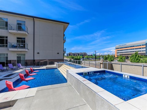 a swimming pool on the roof of a building with red chairs