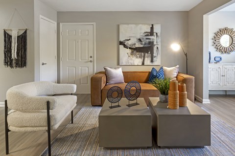A living room with a white chair, a brown couch, and a large painting on the wall.