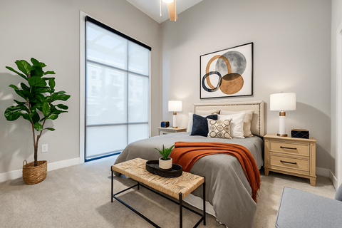 A bedroom with a bed, nightstand, and a plant.