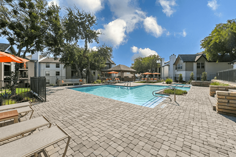 A pool surrounded by a brick patio with a few chairs and umbrellas.