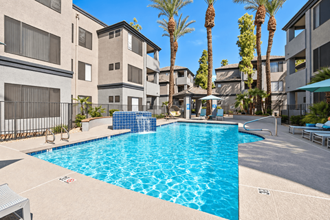 A swimming pool in front of apartment buildings with palm trees.