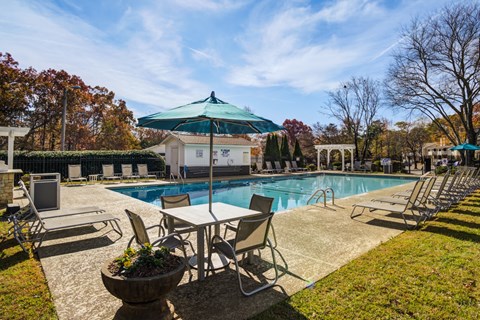 A pool area with chairs and a table under a green umbrella.