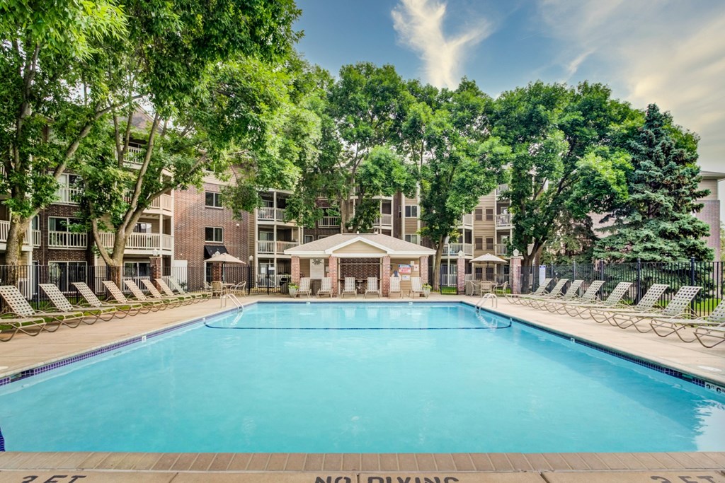 a swimming pool with chaise lounge chairs and trees in front of an apartment building