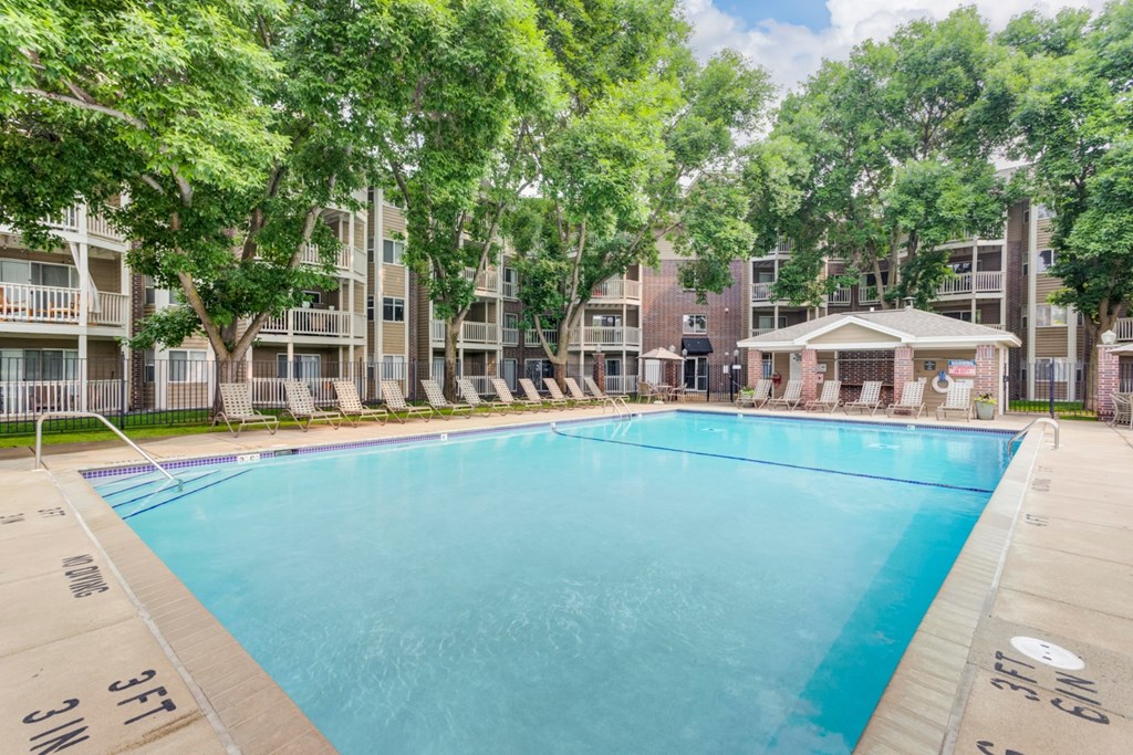 a swimming pool with chaise lounge chairs and trees in front of an apartment building