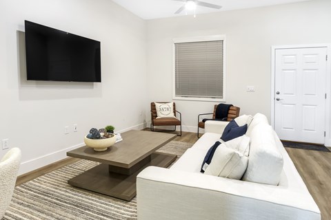 A living room with a white couch and a flat screen TV mounted on the wall.