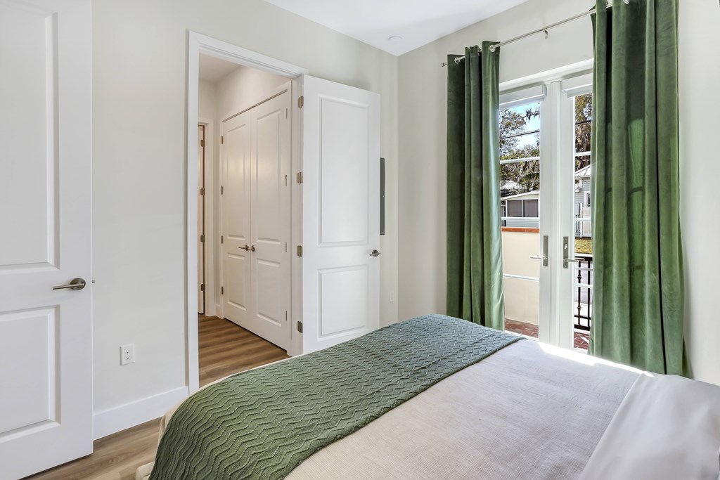 a bedroom with a bed and green curtains and a door to a balcony