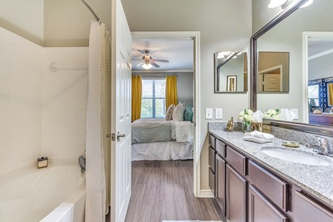 A bathroom with a white tub and a bedroom with a bed and a window.