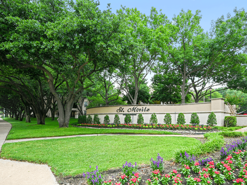 a city with a sign in front of trees and flowers