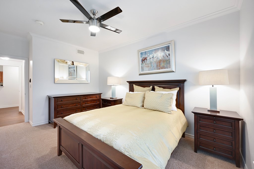 a bedroom with a bed and two dressers and a ceiling fan