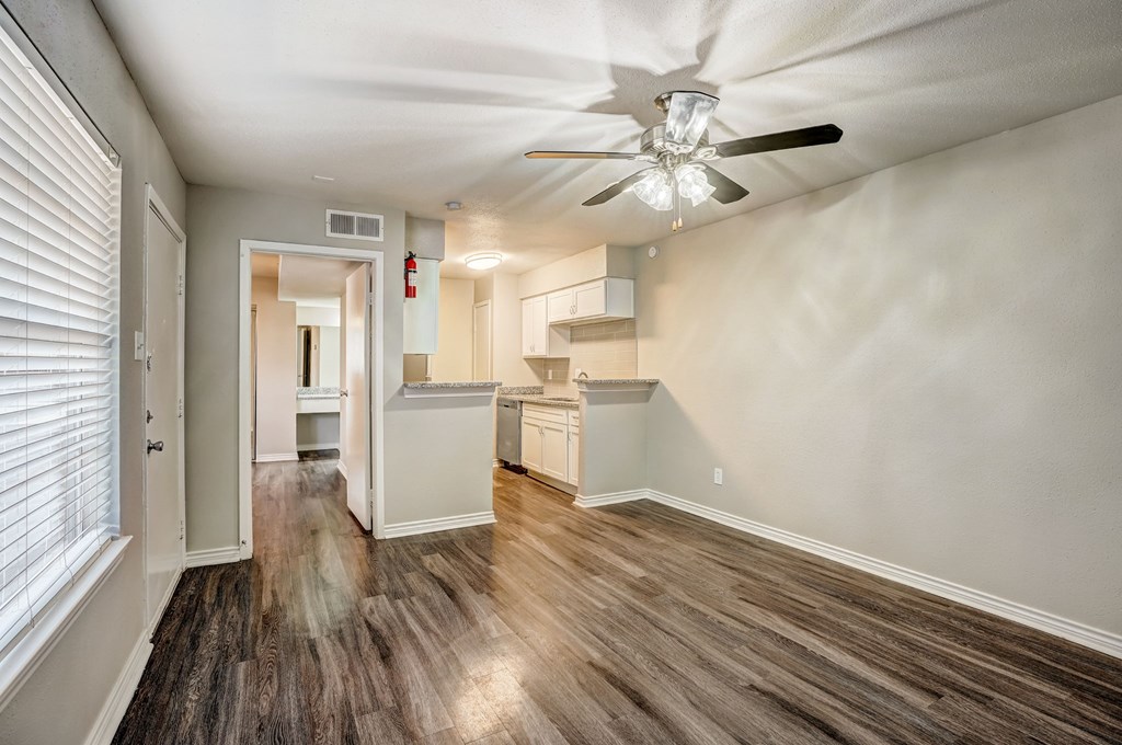 an empty living room with a ceiling fan and a kitchen