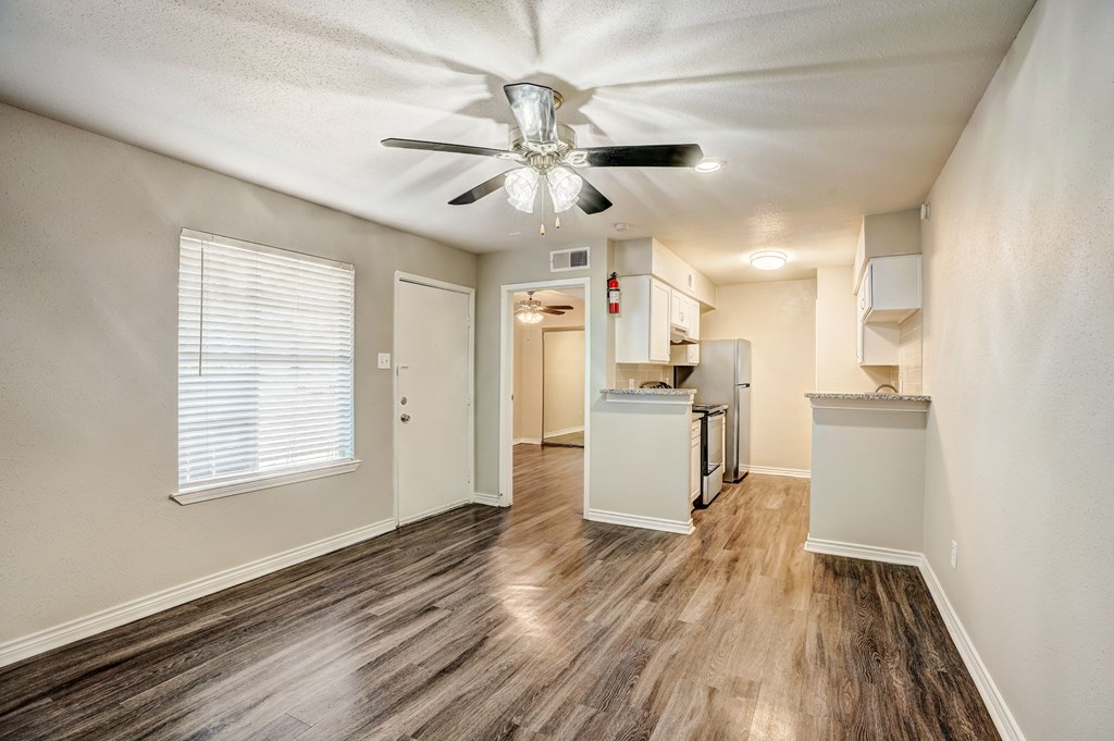 an empty living room with a ceiling fan and a kitchen