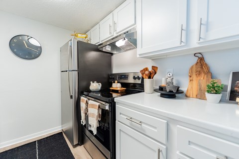 A black refrigerator is in a kitchen with white cabinets.