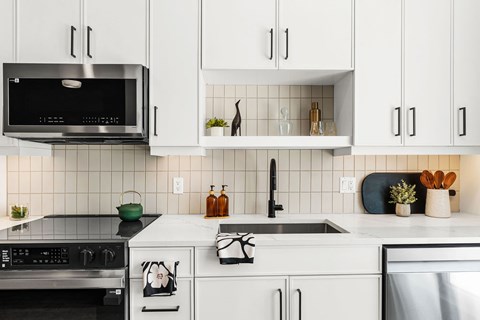 A modern kitchen with white cabinets and black appliances.